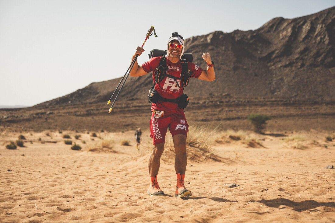 Artur Kujawiński na trasie Marathon des Sables z kijkami uniesionymi w górę